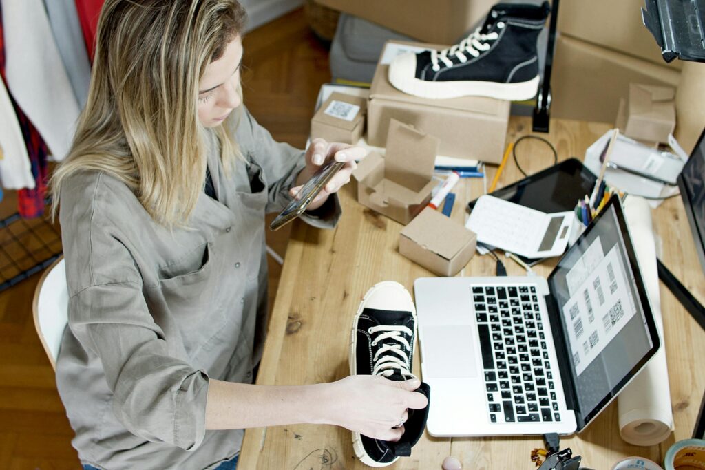 Ecommerce owner packing boxes and using a laptop assistant to write product listings—AI Assistants for Small Business for online stores.