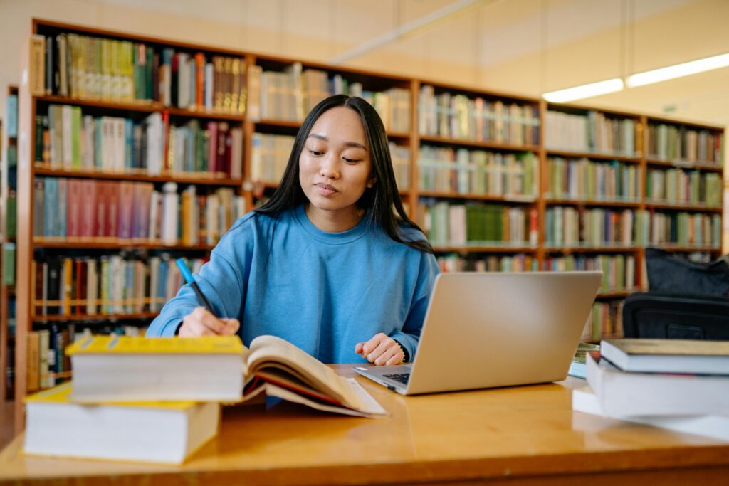 Student using laptop with AI study assistant in library — Best AI Tools for Students 2025.